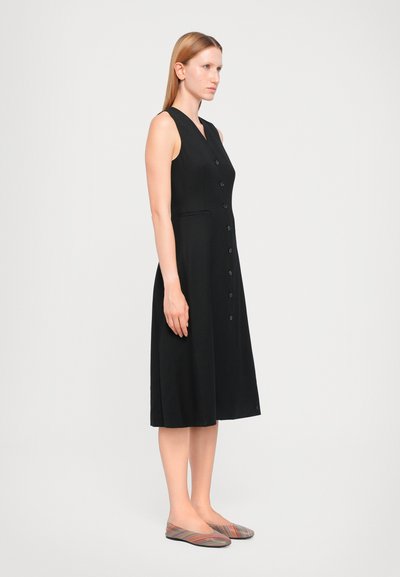 Musthave musta ilma varrukatega kleit sügava V-kaelusega, esiküljel nupud, kaks küljetaskut ja voolav seelik. Seljas mitmevärvilised triibulised lamedad jalanõud.