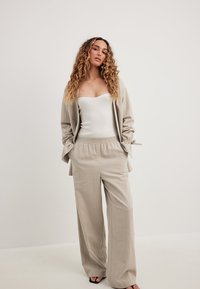 Svetlo bež laneni blejzer in ujemajoči se široki hlače, združeni z oprijetim belim vrhom. Tkanina ima mehak občutek in sproščen kroj.