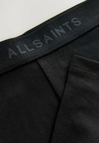Närbild av svart underklädesmidja med "ALLSAINTS"-logotyp präglad, som visar tygstrukturen och sömnadsdetaljer.