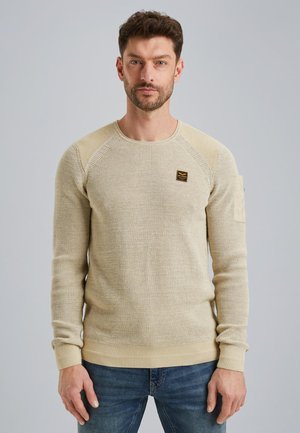 Beige gebreide pullover met een textuurdesign, ronde hals en geribbelde manchetten. Bevat een klein zwart label op de borst en een zijzak.