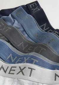 Cinci perechi de lenjerie pentru bărbați prezintă nuanțe variate de albastru, gri și navy, cu brâie elastice gravate cu logo-ul "NEXT".