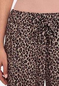 Leopard print pajama pants in light beige with black and pink spots. Features an elastic waistband with a decorative tie and pockets.