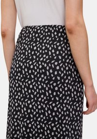 Jupe noire avec un motif de points blancs dispersés. Fabriquée en tissu léger, elle présente une texture lisse et une taille élastique.