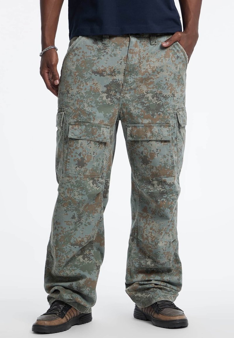 Cargo-Hosen im Tarnmuster mit verschiedenen Grüntönen, Braun und Grau. Lockere Passform mit mehreren Seitentaschen und robustem Stoff.