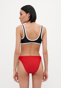 Top de bikini alb-negru cu bretele late, combinat cu un costum de baie tăiat înalt roșu. Textură netedă, design sportiv.
