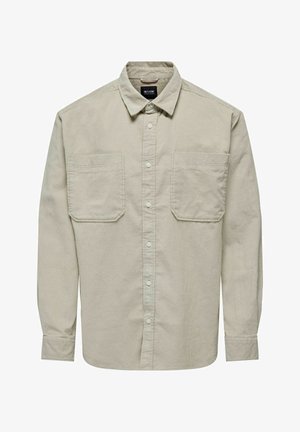 Camisa de corduroy beige de mangas largas con cierre de botones en la parte delantera, dos bolsillos en el pecho y un cuello clásico.