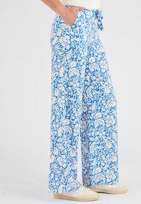 Wijdere broek met een blauw-wit bloemenpatroon, gemaakt van lichtgewicht stof, met zijzakken en een strik tailleband.