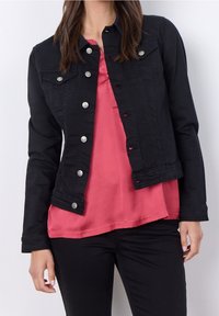 Chaqueta de mezclilla negra con botones plateados, que presenta un collar clásico y bolsillos frontales. Llevada sobre una blusa rosa, con un acabado ligeramente texturizado.