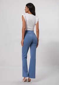Haut blanc côtelé avec des manches bouffantes, associé à un pantalon flare ajusté bleu clair. Les chaussures sont des talons ouverts blancs.