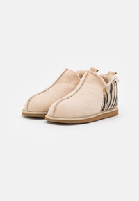 Scarpe slip-on in suede beige con una morbida fodera, dotate di un pannello in tessuto a strisce zebrate su un lato e una suola piatta in gomma.