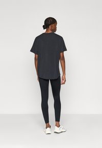 T-shirt noir à manches courtes avec un col arrondi, porté avec des leggings noirs ajustés et des chaussures de sport blanches.