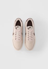 Αθλητικά παπούτσια Nike σε ανοιχτό ροζ με καφέ λεπτομέρειες. Άνω μέρος από λείο δέρμα, στρογγυλή μύτη, σύστημα κορδονιών, επενδυμένος αστράγαλος και το χαρακτηριστικό λογότυπο στη γλώσσα.