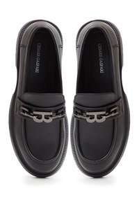 Paire de mocassins en cuir noir avec détail chaîne en métal et nom de la marque imprimé à l'intérieur des chaussures.