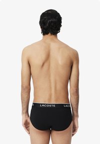 Zwarte slip met een witte 'LACOSTE' logo op de tailleband. Glad materiaal en een snug fit met een laag uitgesneden ontwerp, dat een minimalistische stijl laat zien.