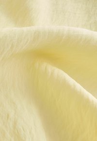 Tissu doux de couleur jaune pâle avec des plis subtils, montrant sa texture et son matériau léger.