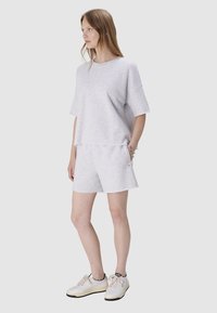 Jasnoszara bawełniana koszulka z luźnym krojem i krótkimi rękawami, zestawiona z dopasowanymi szortami z elastycznym pasem i surowym wykończeniem brzegów.