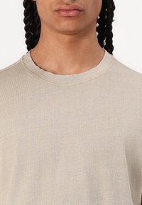 Beige, kortærmet crewneck t-shirt lavet af blødt stof; har en ribbet halsudskæring og subtil tekstur. Rent design uden logoer.