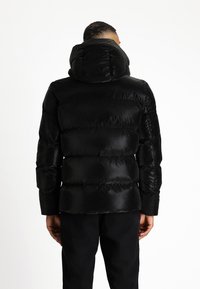 Abrigo de plumas negro con cuello alto y diseño acolchado horizontal. El material parece brillante y tiene una textura suave.