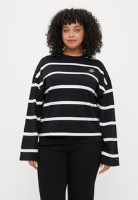 Langærmet skjorte med sort og hvid stribe, rund hals og broderet logo på venstre bryst. Stoffet ser blødt ud og har en afslappet pasform.