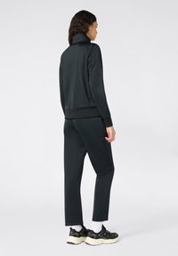 Dres w kolorze czarnym, z wysokim kołnierzem, długimi rękawami i zwężanymi spodniami. Gładka faktura, z kontrastującymi mankietami i dołem.