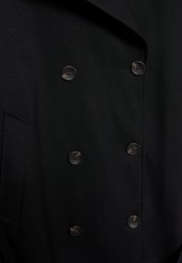 Čierny dvojradový kabát so šiestimi gombíkmi a bočným vreckom, textúrovaná látka a široký golier s klopami.