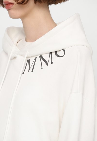 Άσπρη φούτερ μπλούζα από βαμβάκι με μεγάλη μπροστινή τσέπη, ρυθμιζόμενη κουκούλα με κορδόνι και μαύρες λεπτομέρειες εκτύπωσης στο στήθος. Μαλακή υφή.