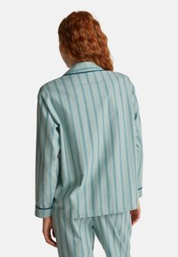 Světle modrý pruhovaný pyžamový set s volným střihem. Obsahuje košili s límečkem a kalhoty v odpovídajícím provedení, vyrobené z měkké látky s jemným leskem.