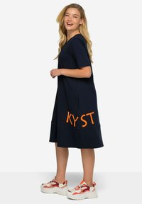 Navy short-sleeve dress with an orange print "KYST" on the lower front, made from a soft material, featuring a flared hemline.