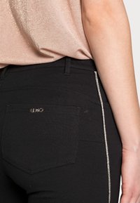 Svarta stretchjeans med en figurnära design, med en rhinstenaccent på sidan och en liten fickdetalj på baksidan.
