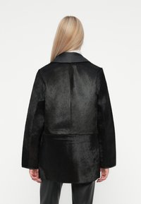 Must must nahktekstiilis mantel, millel on sile must nahk krae, kohandatud lõige ja pikad varrukad. Omab minimalistlikku disaini ja tekstureeritud materjali.