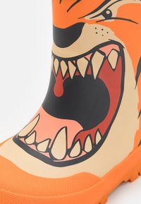 Botte en caoutchouc orange et noire avec un design de visage d'animal féroce, des dents pointues et une semelle texturée pour une meilleure adhérence.