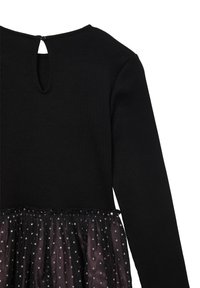 Maglia nera a coste con maniche lunghe e chiusura a bottone a forma di chiave sopra una gonna drappeggiata con sovrapposizione di tulle nero e pois argentati.