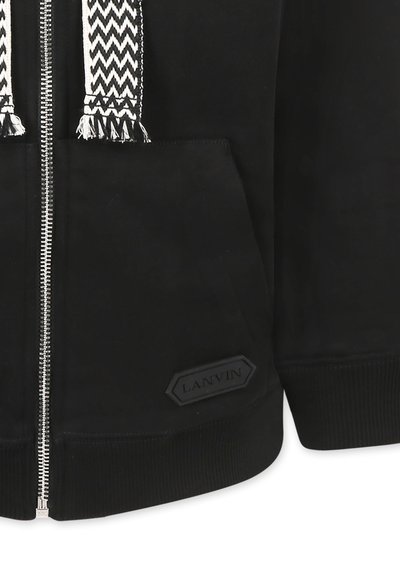 Felpa nera con zip caratterizzata da una tasca testurizzata, polsini a costine e un laccio a trama nera e bianca. Patch con logo sul bordo.