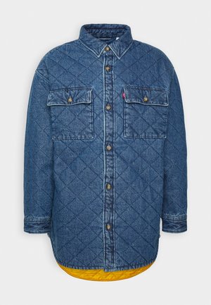 Quilted blue denim jacket with button closure, two front flap pockets, long sleeves, and a visible yellow inner lining at the hem.