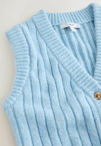 Gaiši zilas bezpiedurkņu veste ar ribotu tekstūru, ar zelta nokrāsas pogu detaļām. Izgatavota no mīksta adīta materiāla.