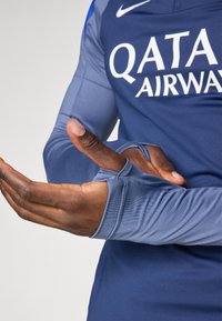 Long-sleeve athletic top in dark blue and light blue, featuring thumbholes, made from smooth, stretchy fabric with a printed logo.