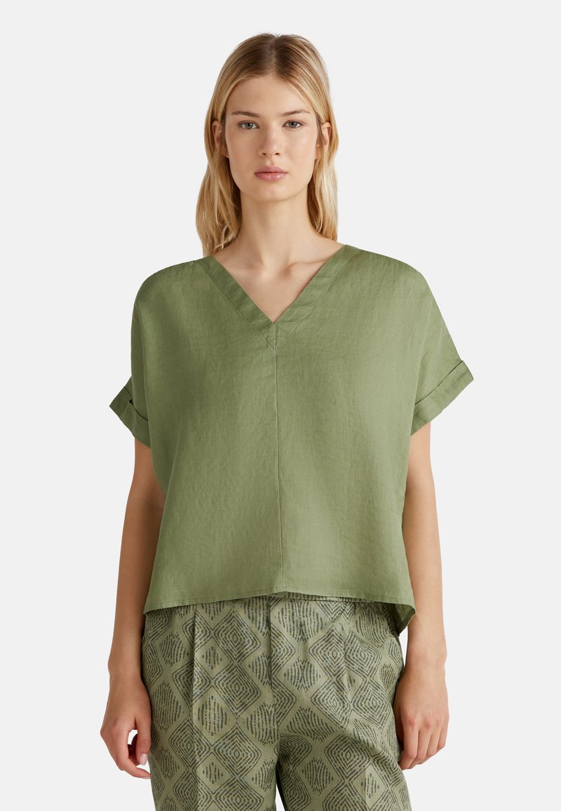 Top verde in lino a V con maniche corte arrotolate, abbinato a pantaloni verdi a fantasia con un design a rombi in verde scuro.