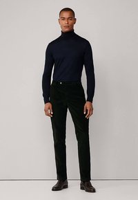 Jersey de cuello alto azul marino oscuro, ajuste ajustado, tejido texturizado. Pantalones de pana verdes, corte recto, brillo sutil. Botas de cuero marrón, diseño sencillo.