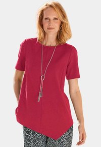 Fuchsia-Oberteil mit kurzen Ärmeln und rundem Ausschnitt. Verfügt über einen asymmetrischen Saum und eine lange silberne Halskette mit Quasten.