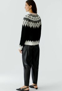 Un pull à motif noir et blanc avec une texture duveteuse, associé à un pantalon en cuir noir et des chaussures plates noires.