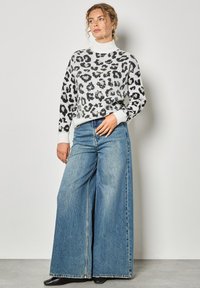 Sweter dzianinowy w białej bazie z czarnym wzorem w panterkę. W zestawieniu z szerokimi, niebieskimi dżinsami. Miękka tekstura, luźny krój i wysoka stójka.
