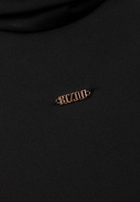 Zwarte stof met een gladde textuur heeft een goudkleurige metalen speld met de tekst "BIZUU" die in het midden is bevestigd.