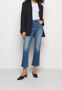 Blazer negro a rayas sobre una camiseta blanca, combinado con jeans acampanados de color azul claro y zapatillas de tacón negras. Colores claros y formas estructuradas.