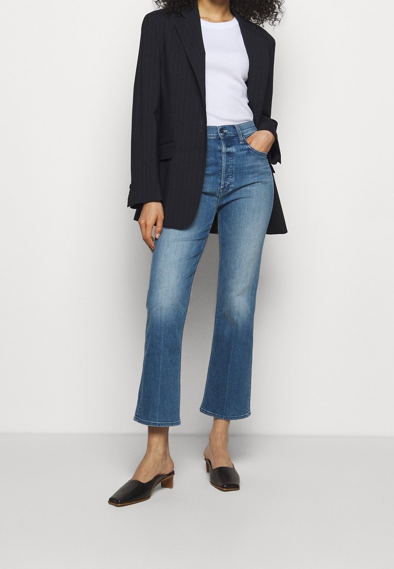 Blazer negro a rayas sobre una camiseta blanca, combinado con jeans acampanados de color azul claro y zapatillas de tacón negras. Colores claros y formas estructuradas.