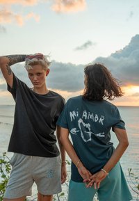 Dva pojedinca nose ležernu odjeću. Jedan nosi tamnu majicu, a drugi tirkiznu majicu s bijelim natpisom. Oba nose kratke hlače različitih uzoraka.