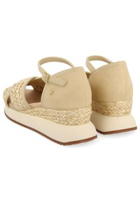 Sandalias beige con laterales de paja trenzada, parte superior lisa y un tacón grueso con una suela de goma ligera. Correa ajustable en el tobillo con hebilla.