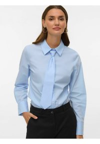 Camisa de botones azul claro con corbata, mangas largas, cuello puntiagudo, textura suave, combinada con pantalones negros. Diseño simple y clásico.