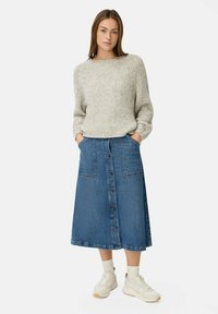 Un pull en tricot gris clair à texture côtelée associé à une jupe en jean bleu arrivant au genou avec des boutons sur le devant et deux poches. Des baskets blanches complètent le look.
