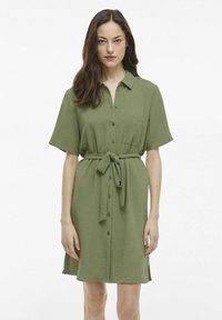 Trumpo rankovėmis, alyvuogių spalvos suknelė marškinėliais su mygtukais, apykakle ir diržu, pagaminta iš tekstūruoto audinio ir turinti šoninius plyšius.