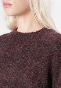 Maglione in lana bordeaux con scollo rotondo, lavorazione a maglia testurizzata e macchie colorate. Primo piano dei dettagli del tessuto e delle cuciture.